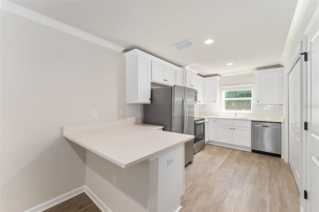 9011 N Travis Dr, Citrus Springs, FL 34434 - kitchen featuring stainless steel appliances, a peninsula, tasteful backsplash, light wood finished floors, and white cabinetry