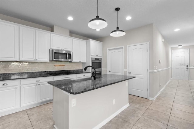 1011 Wetland Ridge Cir, Middleburg, FL 32068 - kitchen with stainless steel appliances, light tile patterned floors, white cabinets, backsplash, and a kitchen island with sink