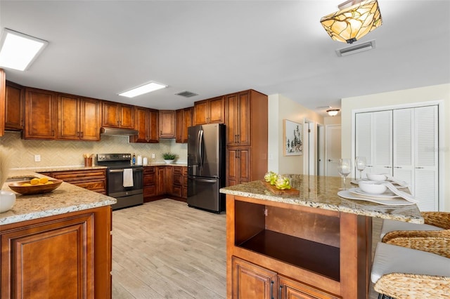 900 NW Snug Harbor Rd, Crystal River, FL 34428 - kitchen featuring stainless steel appliances, under cabinet range hood, light stone counters, light wood-type flooring, and tasteful backsplash