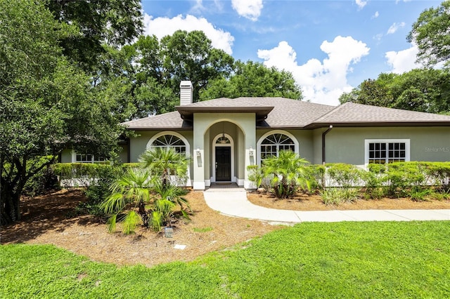 2013 SW 76th Ter, Gainesville, FL 32607 - view of front of home featuring stucco siding, a front lawn, a chimney, and roof with shingles