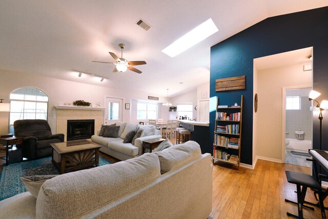 3735 NW 64th Pl, Gainesville, FL 32653 - living room featuring vaulted ceiling, a ceiling fan, light wood-type flooring, a tiled fireplace, and a skylight