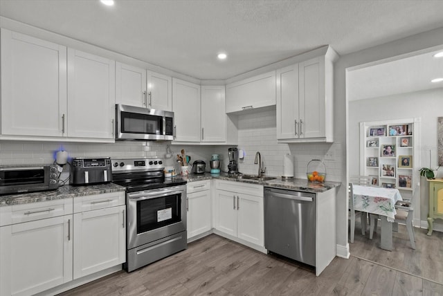 4444 5th Ave S, Saint Petersburg, FL 33711 - kitchen featuring appliances with stainless steel finishes, white cabinets, dark stone countertops, tasteful backsplash, and light wood-style flooring