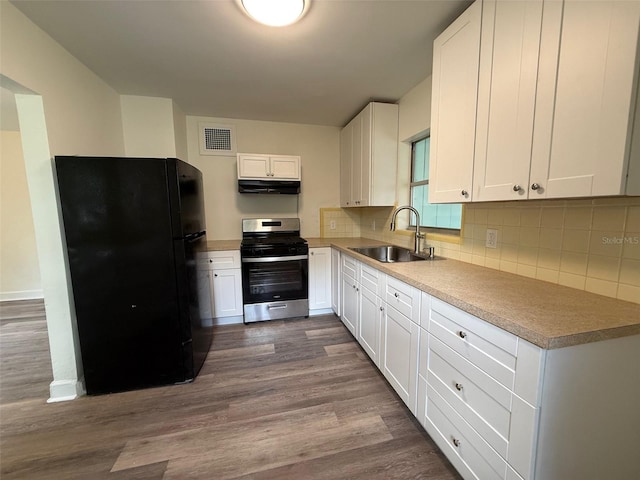 926 NW 24th Ave, Gainesville, FL 32609 - kitchen with stainless steel gas stove, freestanding refrigerator, under cabinet range hood, white cabinetry, and dark wood-style floors