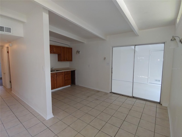 2904 NE 11th Ter, Gainesville, FL 32609 - kitchen featuring beam ceiling, light tile patterned floors, brown cabinetry, and light countertops