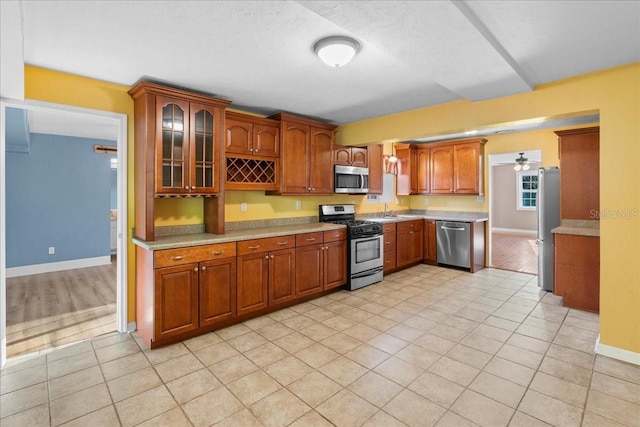 3404 NW 4th St, Gainesville, FL 32609 - kitchen with stainless steel appliances, light countertops, light tile patterned floors, glass insert cabinets, and brown cabinetry
