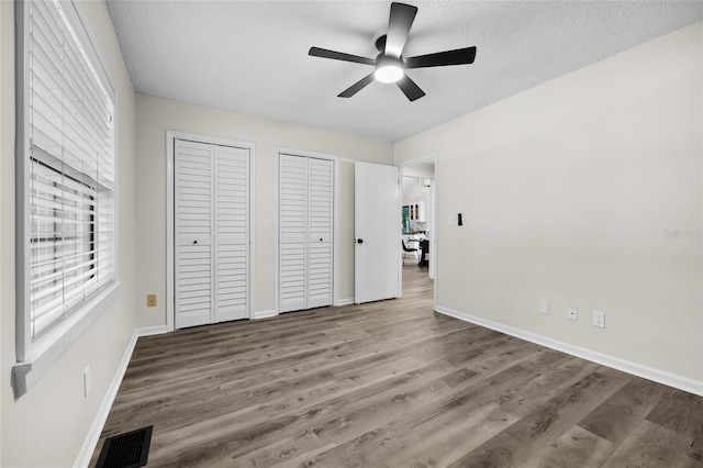 2101 SW 79th Dr, Gainesville, FL 32607 - unfurnished bedroom featuring two closets, wood finished floors, a textured ceiling, and a ceiling fan