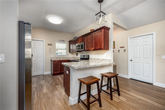 25111 SW 6th Ln, Newberry, FL 32669 - kitchen featuring appliances with stainless steel finishes, a peninsula, wood finished floors, lofted ceiling, and a kitchen breakfast bar