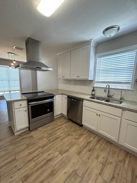 3372 Penny Ln, Middleburg, FL 32068 - kitchen featuring appliances with stainless steel finishes, island range hood, light wood-style flooring, white cabinets, and a textured ceiling