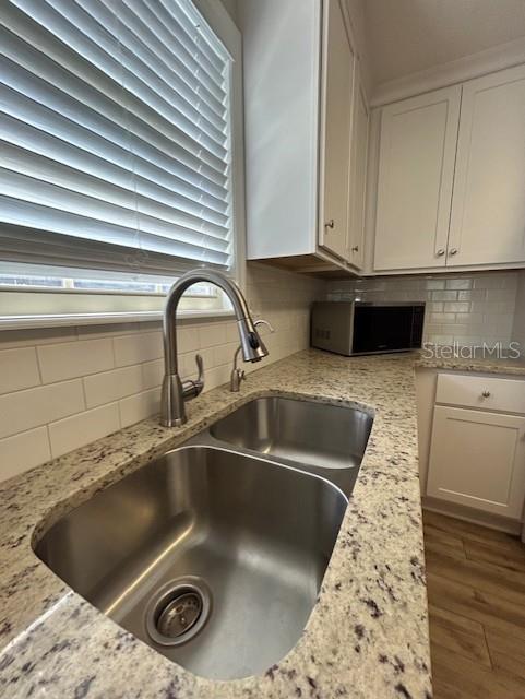 3372 Penny Ln, Middleburg, FL 32068 - kitchen view of stainless steel microwave, tasteful backsplash, wood finished floors, white cabinets, and light stone countertops