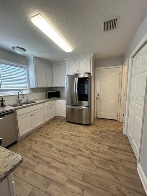 3372 Penny Ln, Middleburg, FL 32068 - kitchen with stainless steel appliances, white cabinetry, light wood-style flooring, a textured ceiling, and light stone counters
