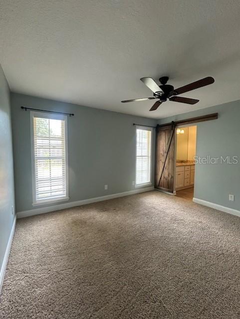 3372 Penny Ln, Middleburg, FL 32068 - empty room featuring light carpet, a ceiling fan, a barn door, and a textured ceiling