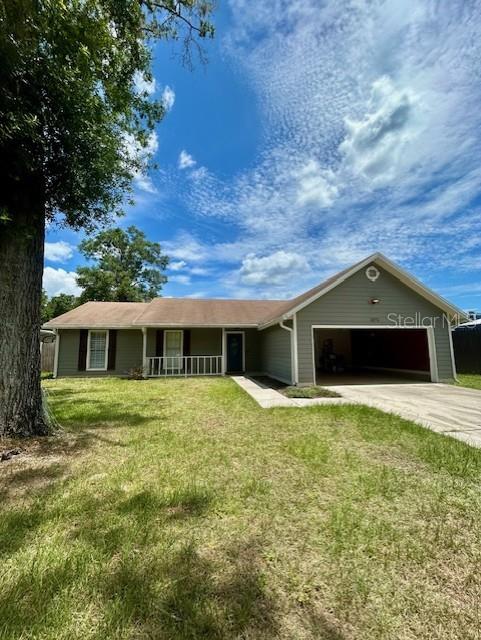 3372 Penny Ln, Middleburg, FL 32068 - ranch-style house with an attached garage, covered porch, a front lawn, and driveway
