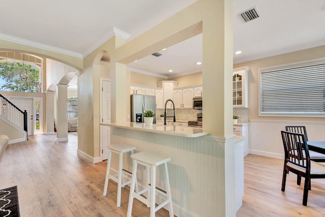 6364 Golden Eye Gln, Lakewood Ranch, FL 34202 - kitchen featuring stainless steel appliances, a kitchen breakfast bar, arched walkways, backsplash, and light wood-style floors