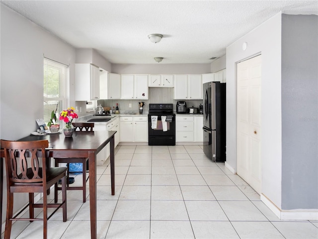2826 NE 18th Ct, Ocala, FL 34470 - kitchen featuring black / electric stove, freestanding refrigerator, white cabinetry, light tile patterned floors, and a textured ceiling