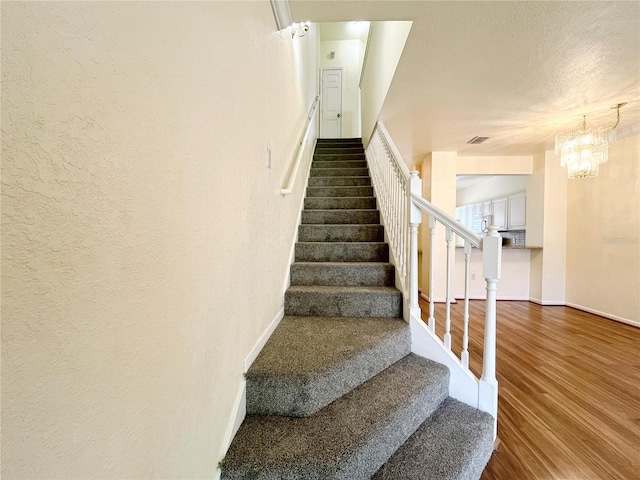 4877 NW 42nd Rd Unit 106, Gainesville, FL 32606 - stairway featuring wood finished floors, a chandelier, and a textured wall