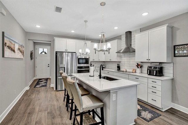 kitchen featuring baseboards, visible vents, wall chimney exhaust hood, appliances with stainless steel finishes, and a sink