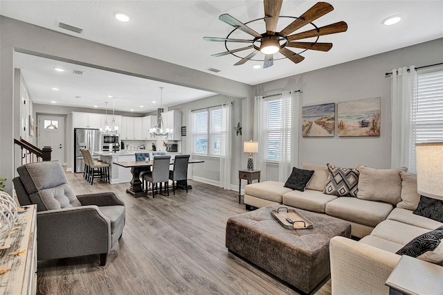 living room with baseboards, recessed lighting, light wood-style flooring, visible vents, and ceiling fan with notable chandelier