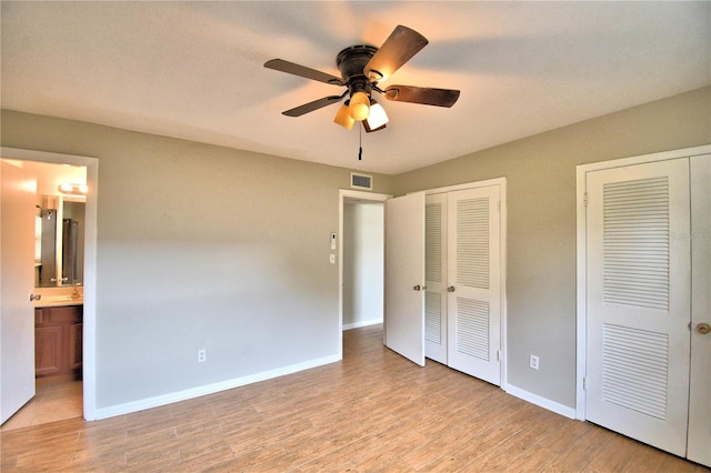 unfurnished bedroom with light wood-type flooring, ensuite bathroom, baseboards, visible vents, and two closets