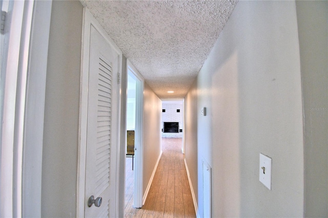 hall with baseboards, visible vents, a textured ceiling, and light wood-style flooring