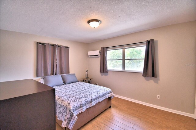 bedroom featuring baseboards, a wall mounted AC, wood finished floors, and a textured ceiling