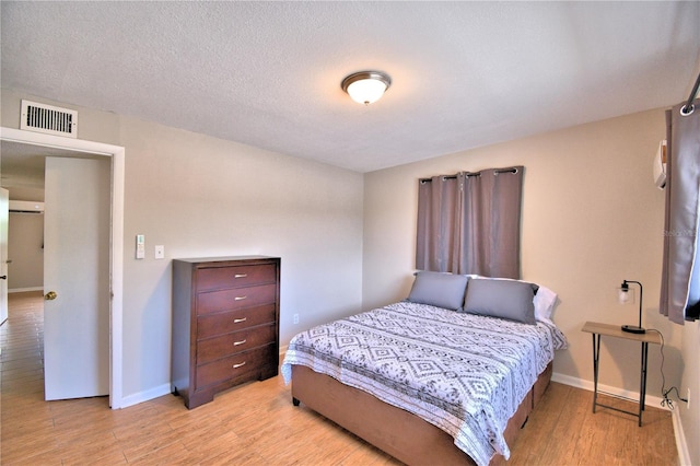 bedroom featuring baseboards, visible vents, wood finished floors, and a textured ceiling