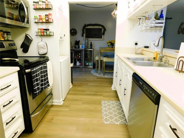 kitchen with sink, white cabinets, appliances with stainless steel finishes, washer / clothes dryer, and light wood-type flooring