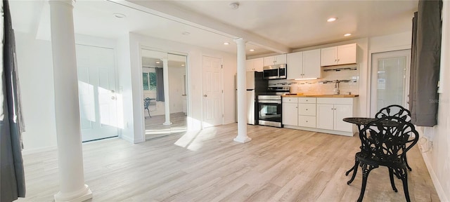 kitchen with appliances with stainless steel finishes, sink, decorative columns, and white cabinets