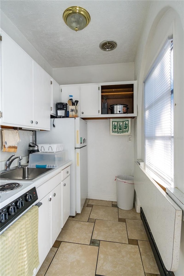 kitchen with sink, a textured ceiling, white cabinets, light tile patterned flooring, and white fridge