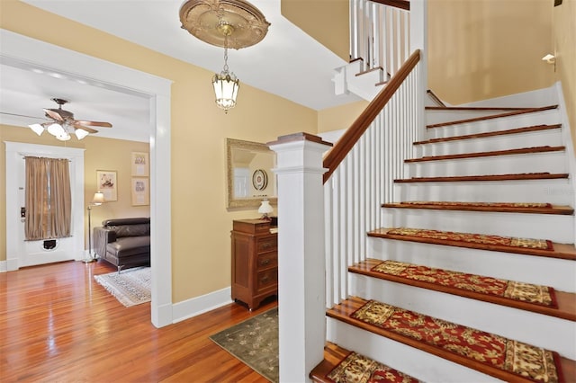 stairs with hardwood / wood-style floors and ceiling fan with notable chandelier