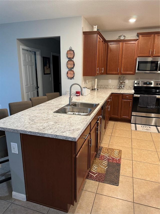 kitchen with a breakfast bar, sink, light tile patterned flooring, kitchen peninsula, and stainless steel appliances