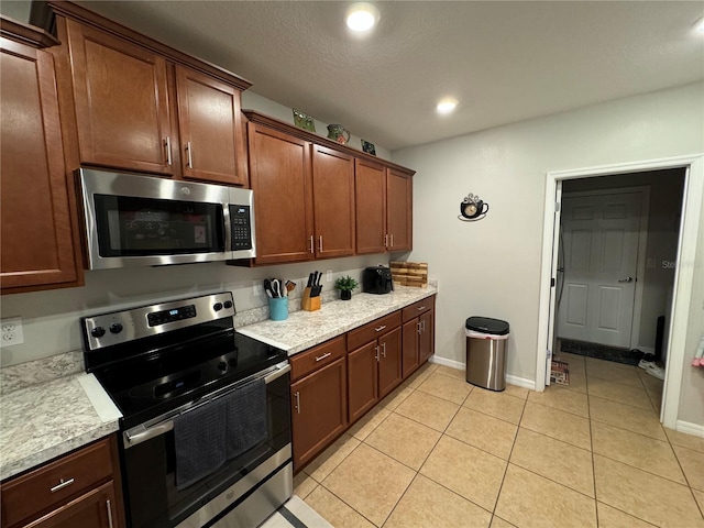 kitchen with light stone countertops, light tile patterned floors, a textured ceiling, and stainless steel appliances