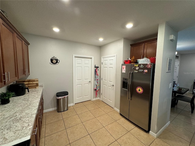 kitchen with stainless steel fridge with ice dispenser, light stone counters, and light tile patterned flooring