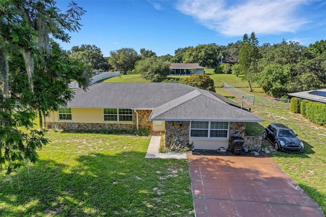 ranch-style home featuring stone siding, a front lawn, a shingled roof, and driveway