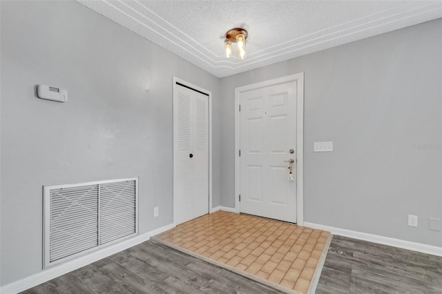 entrance foyer with a textured ceiling, wood finished floors, visible vents, and baseboards