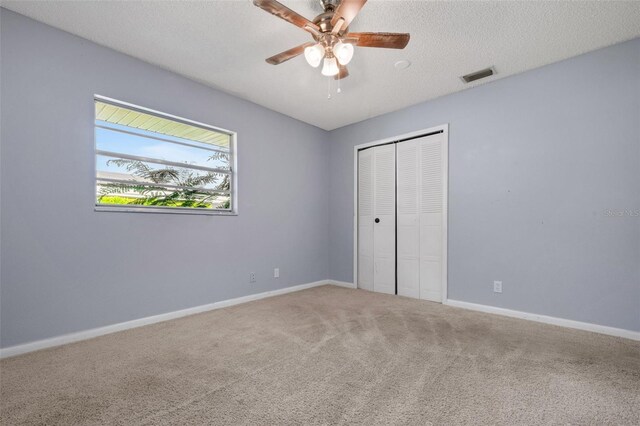 unfurnished bedroom featuring a textured ceiling, visible vents, baseboards, a closet, and carpet