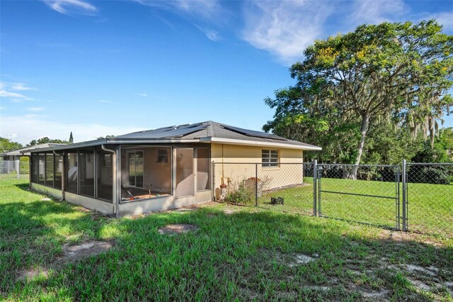 back of property featuring solar panels, fence, a sunroom, a yard, and a gate