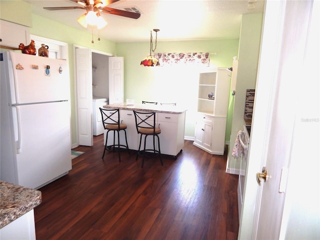 kitchen with decorative light fixtures, white cabinets, a kitchen bar, white fridge, and dark wood-type flooring