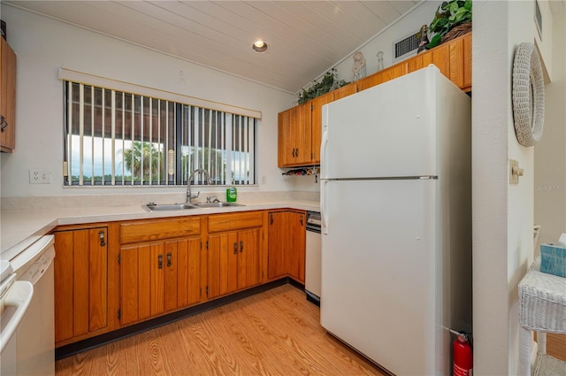 kitchen featuring lofted ceiling, white appliances, a sink, light wood-style floors, and light countertops