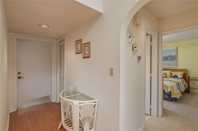 hall featuring arched walkways, wood finished floors, a textured ceiling, and carpet flooring