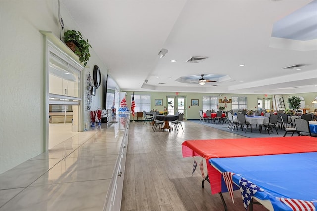 recreation room featuring a tray ceiling, light hardwood / wood-style floors, and ceiling fan