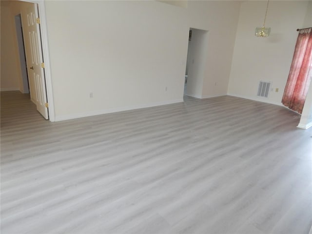 empty room featuring a notable chandelier, light wood-type flooring, visible vents, and baseboards