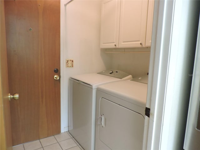 clothes washing area featuring separate washer and dryer, light tile patterned floors, and cabinets