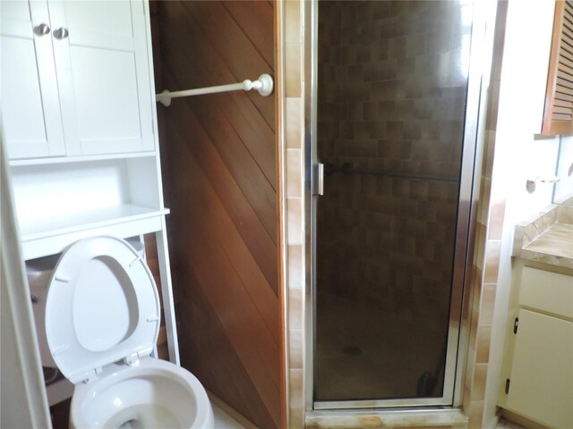 bathroom featuring vanity, toilet, a shower with shower door, and wood walls