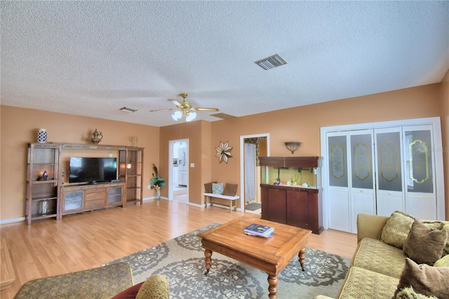 living room featuring ceiling fan, a textured ceiling, and light wood-type flooring