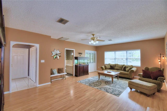 living room with light hardwood / wood-style flooring, ceiling fan, and a textured ceiling