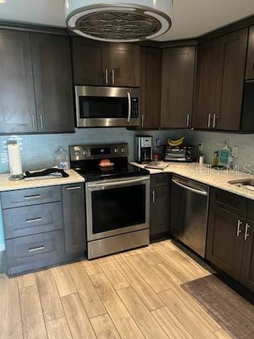 kitchen with dark brown cabinets, light hardwood / wood-style floors, appliances with stainless steel finishes, and tasteful backsplash