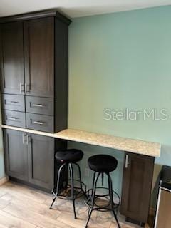 bar featuring dark brown cabinets and light hardwood / wood-style floors