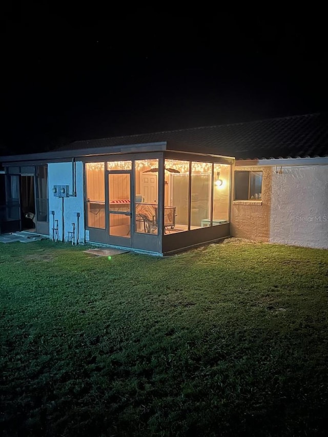 back house at night featuring a yard and a sunroom