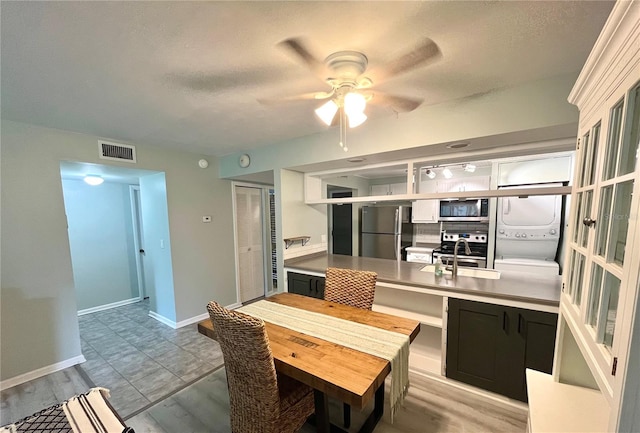 kitchen with stacked washer / dryer, appliances with stainless steel finishes, light wood-type flooring, and ceiling fan