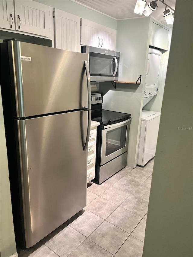 kitchen featuring light tile patterned floors, white cabinetry, stacked washing maching and dryer, and stainless steel appliances